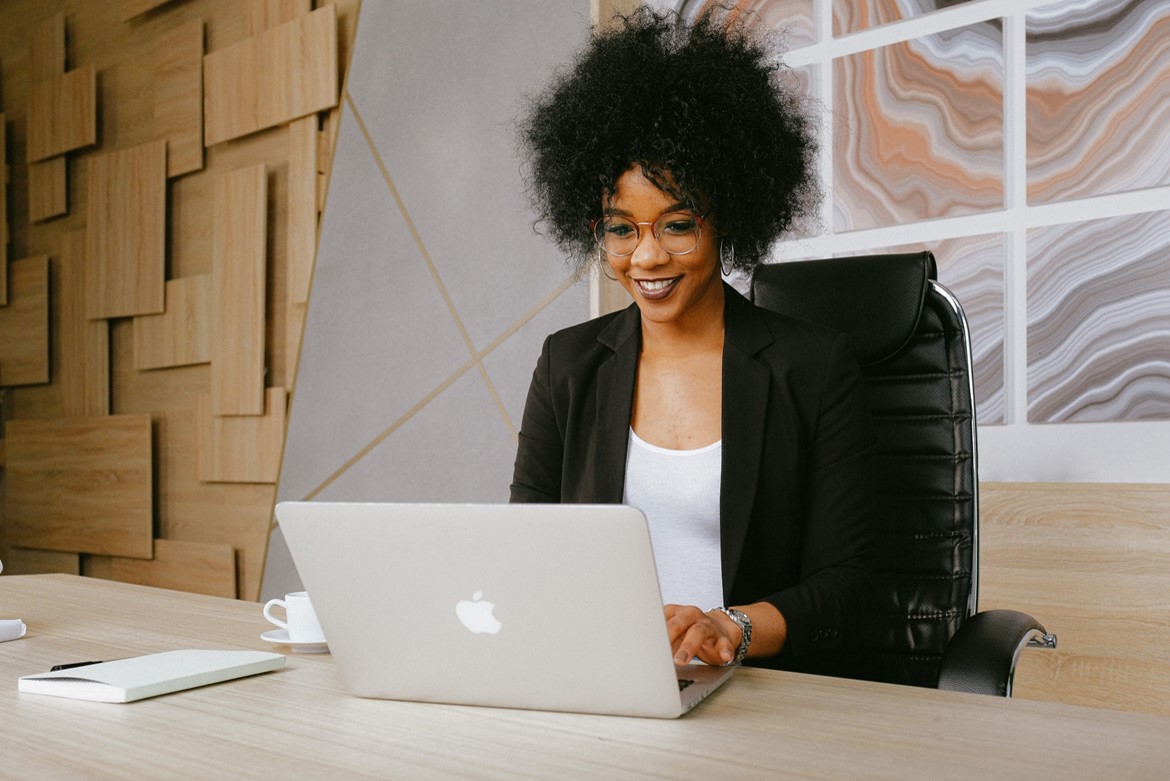 black woman wearing a black blazer sitting by the table while using laptop